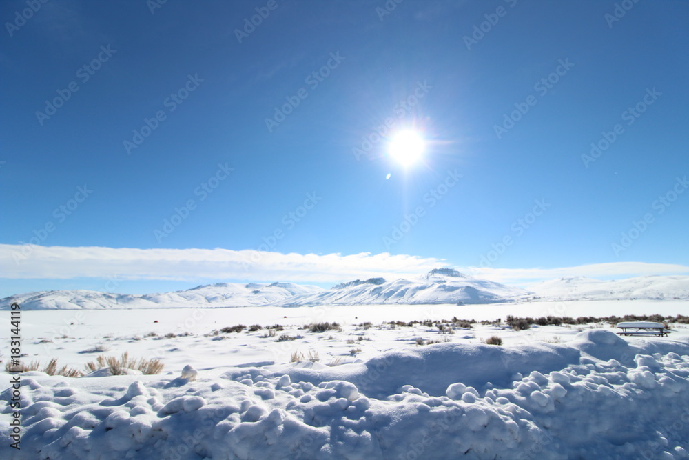 Wide open landscape covered in thick snow with sun in the horizon Wide open landscape covered in thick snow with sun in the horizon