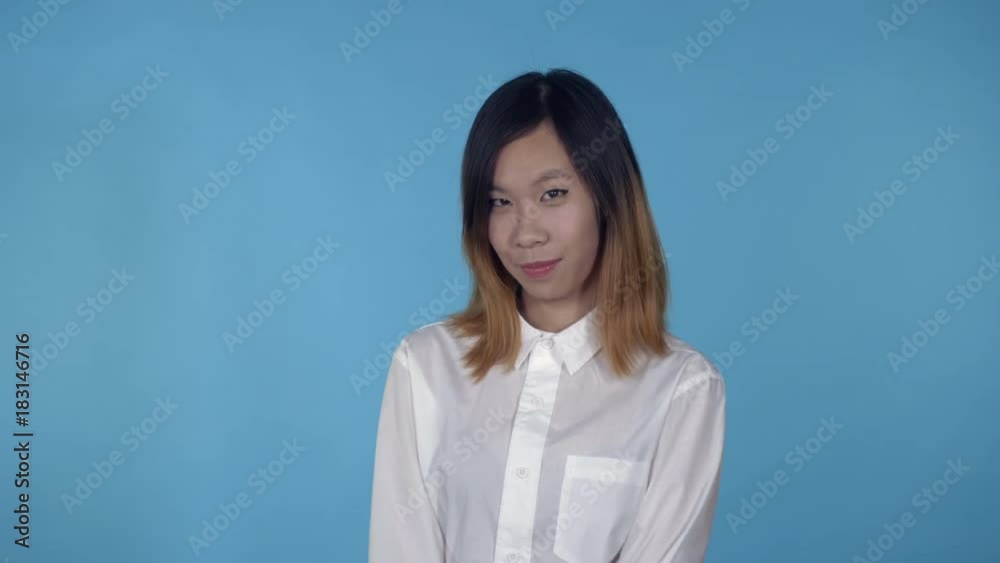 young asian woman posing flirting on blue background in studio. attractive millennial girl wearing white casual shirt looking at the camera smiling young asian woman posing flirting on blue background in studio. attractive millennial girl wearing white casual shirt looking at the camera smiling