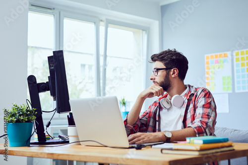 Focused young man thinking about his start-up business while looking at screen in home office