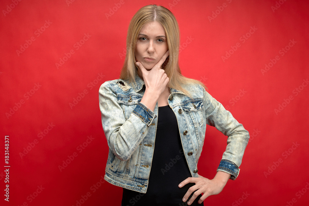 portrait on a red background in the Studio of a young long-haired woman in a denim jacket with an expressive look at the camera. expression pensive and evaluates portrait on a red background in the Studio of a young long-haired woman in a denim jacket with an expressive look at the camera. expression pensive and evaluates
