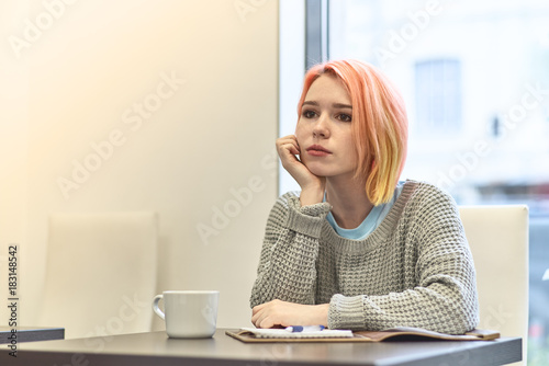 lonely bored young girl sitting at a table in a cafe, leaning her head on his hand with a sad upset depressed expression