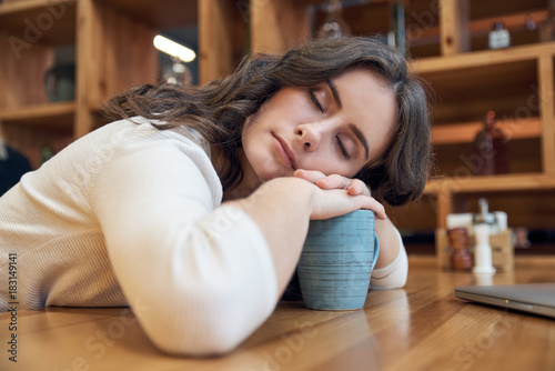 Attractive long-haired girl tiredly falls asleep at a table in a cafe. The concept of morning awakening, tiredness, insomnia, long wait, not the vigor