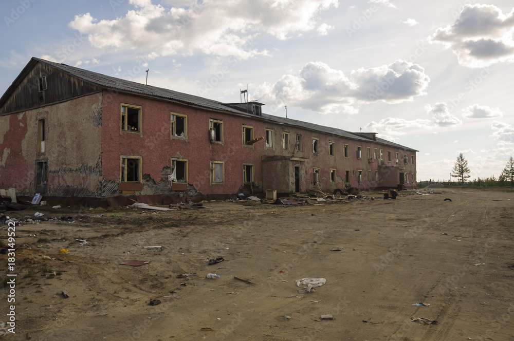 Old two-storied destroyed red house in autumn with sand around. Poverty and misery, North