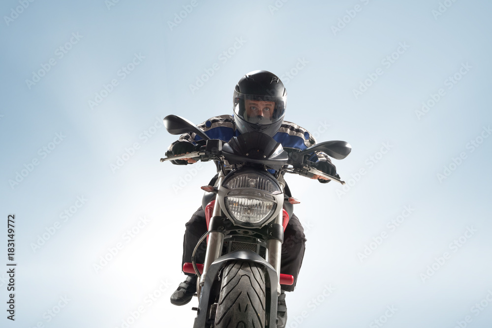 Fototapeta premium Biker in black jacket and helmet sitting on his sportive bike on blue background