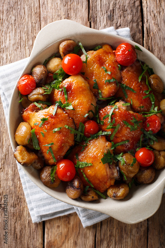 Fried chicken with chestnuts, greens and tomatoes close-up in a bowl. Vertical top view