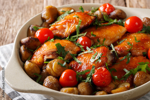 Fried chicken with chestnuts, greens and tomatoes close-up in a bowl. horizontal