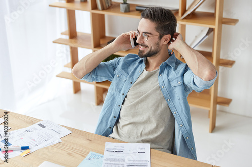 Smiling carefree male financier or freelancer works remotely, has coversation with girlfriend, invites her on romantic dinner, wants to have rest after working on documents. Technology, career concept photo