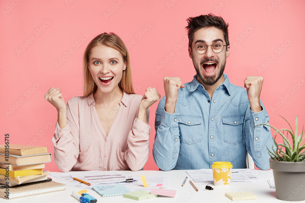Two successful female and male students rejoice to finish working at project, raise and clench fists, have happy expressions, glad to reach goals. Partners work on common report, have good results Two successful female and male students rejoice to finish working at project, raise and clench fists, have happy expressions, glad to reach goals. Partners work on common report, have good results