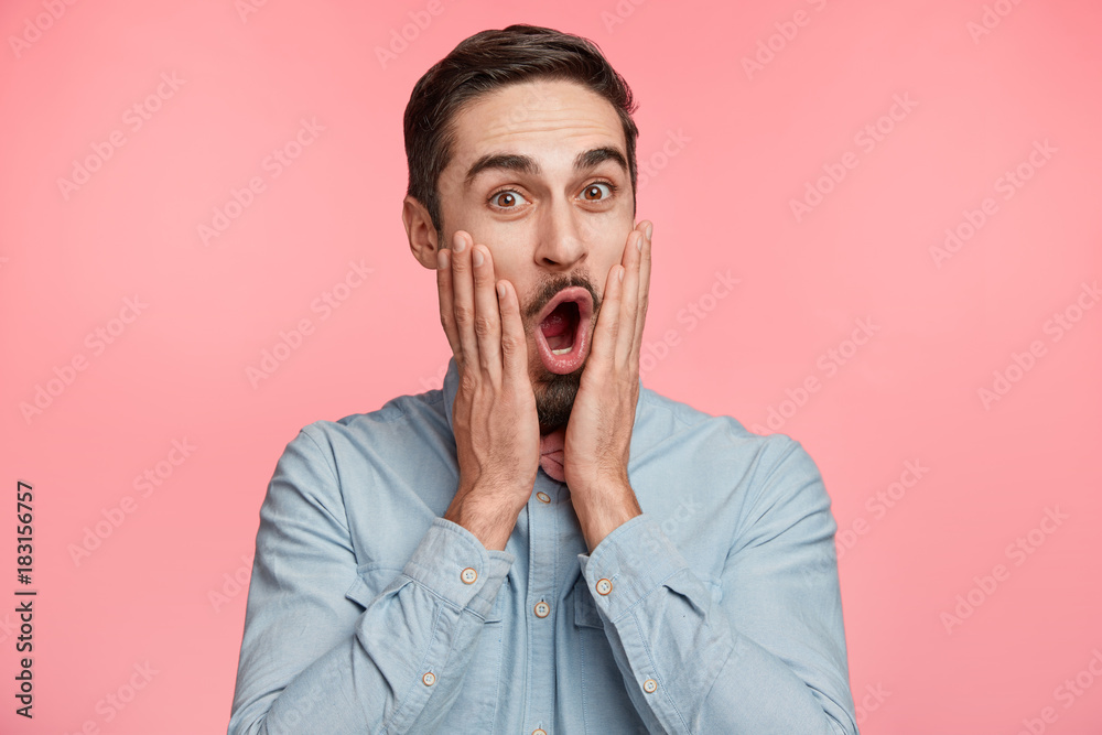 Portrait of satisfied amazed man with beard, opens mouth says wow, being astonished to see something, keeps hand on cheeks, isolated over pink background. People, reaction and emotions concept Portrait of satisfied amazed man with beard, opens mouth says wow, being astonished to see something, keeps hand on cheeks, isolated over pink background. People, reaction and emotions concept