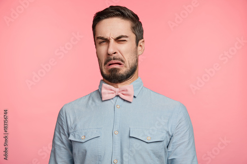 Ugh, how disgusting! Displeased unshaven young male dressed formally, says fie and has dissatisfied facial expression as sees something abominable or detestable, isolated over pink studio background photo