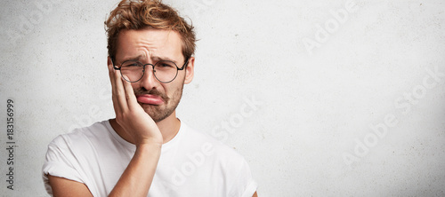 Tableau sur toile Discontent sorrorful male has terrible toothache, can`t stand pain, being upset, poses against white background with copy space for your advertising content