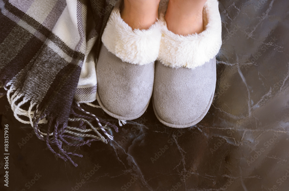 Female legs in cozy slippers on mramor  floor with cashmere blanket. Woman wearing  warm and comfortable slippers on the morning. Relax and stay at home concept. Copy space. - obrazy, fototapety, plakaty 