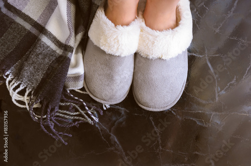 Female legs in cozy slippers on mramor  floor with cashmere blanket. Woman wearing  warm and comfortable slippers on the morning. Relax and stay at home concept. Copy space. photo