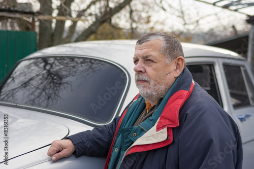 Nice portrait of senior man standing near his old car