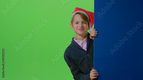 Teen in christmas hat with bubon appears from the side boards on a green screen photo