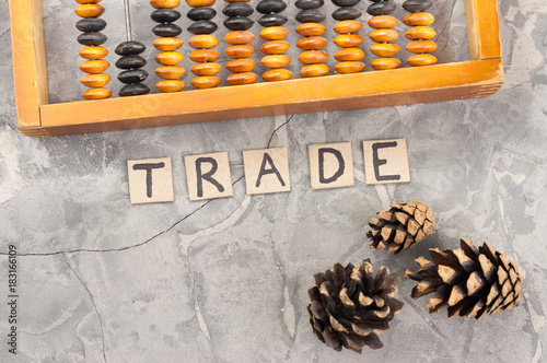 Word TRADE laid out of handwritten letters on cardboard squares near old wooden abacus and three cones on gray cracked concrete