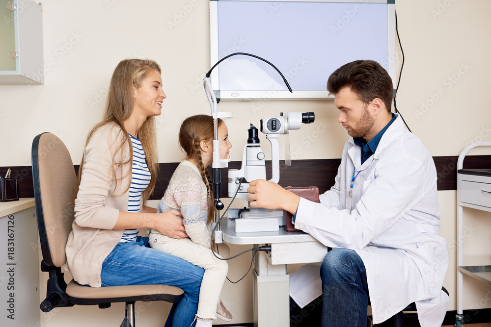 Side view portrait of optometrist testing sight of smiling little girl using slit lamp during medical check up in eye clinic