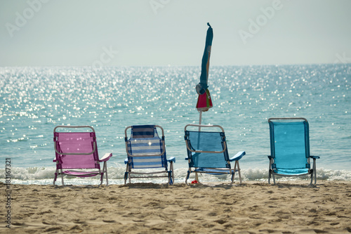 Close-up view of four colorful hammocks and one closed umbrella in an empty sand beach against the calm sea horizon on sunny day