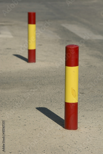 Red and yellow bollards with painting chips on dirty asphalt