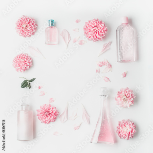 Pastel pink cosmetic product setting flat lay with flowers on white desk background, top view, frame. Layout for skin care, wellness or spa and beauty concept