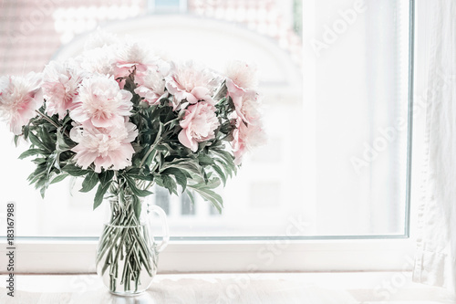 Beautiful pastel pink bouquet of peonies in glass vase on windowsill. Flowers in interior design. Cozy home.