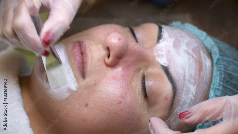 Female cosmetologist making cosmetic facial mask to the female client at the cosmetology centre. Face cleaning Female cosmetologist making cosmetic facial mask to the female client at the cosmetology centre. Face cleaning