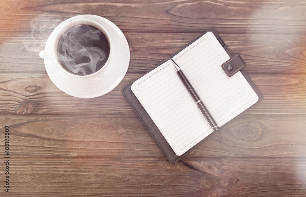 cup of coffee, notebook with pen on a wooden background