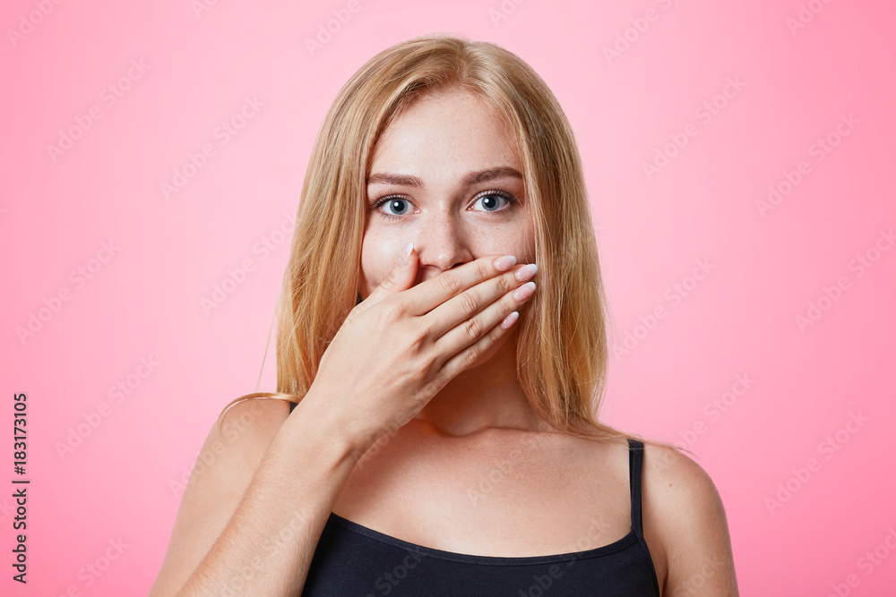 Plesant looking light haired female dressed casually, covers mouth with hand, tries to keep silent and not tell secret, isolated over pink studio background. People, beauty, body language concept Plesant looking light haired female dressed casually, covers mouth with hand, tries to keep silent and not tell secret, isolated over pink studio background. People, beauty, body language concept