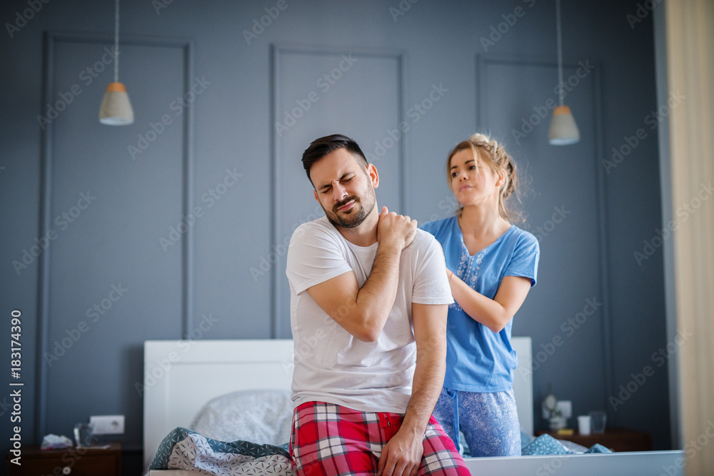 Tired unhappy man holding his neck after bad sleep while his wife looking sadly to him and helping with massage. Tired unhappy man holding his neck after bad sleep while his wife looking sadly to him and helping with massage.