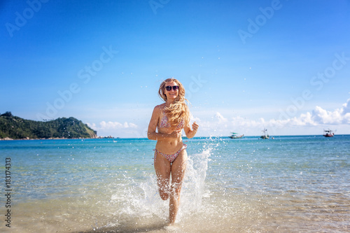 Beautiful young woman with long hair runs along a tropical beach, splashes of water. Happiness, joy, vacation and travel concept © olezzo