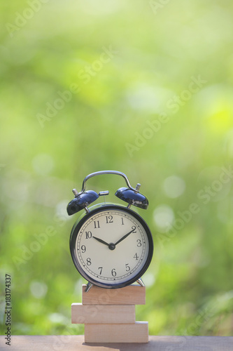 Black alarm clock stacked on wooden bar with shallow DOF green background. Business / Time Management concept.