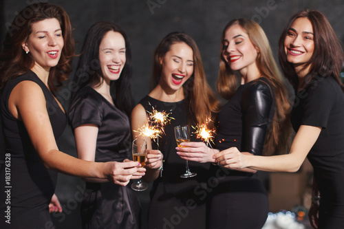 Beautiful girls in evening dresses with glasses of champagne to celebrate the New year, holding sparklers