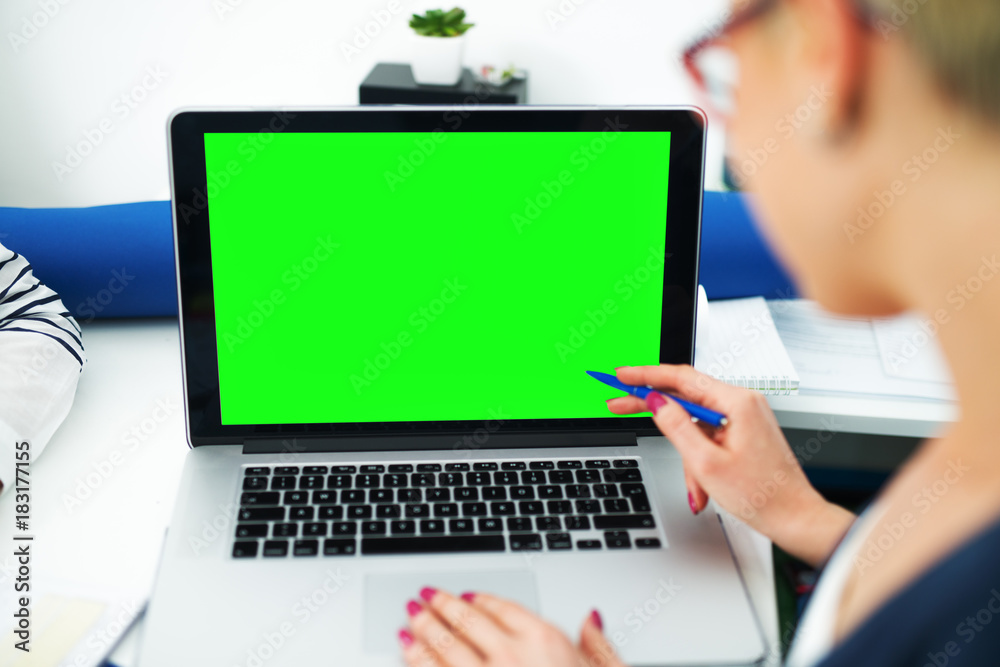Rear view of woman with pencil showing on a laptop with a blank green editable screen in the office. Rear view of woman with pencil showing on a laptop with a blank green editable screen in the office.