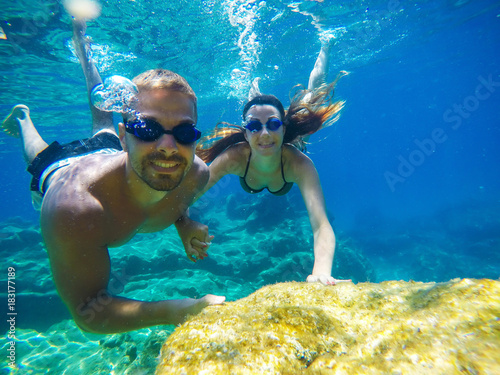 Underwater photo of a young tourist love couple swimming in the turquoise sea under the surface near coral reef while holding hands together for summer vacation.