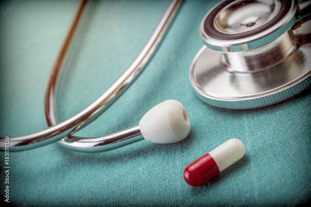 Red and white capsule next to a stethoscope, conceptual image Red and white capsule next to a stethoscope, conceptual image