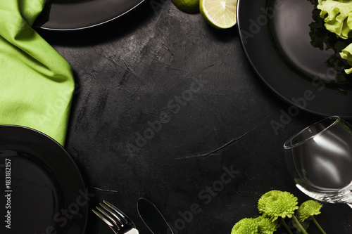 Plates and cutlery on black background with contrast green color. Creative fancy restaurant table setting. Art and design concept photo