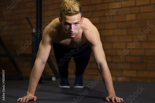 Athlete with a beautiful body and a naked torso doing push-ups exercise on the floor. Studio shot in a dark tone.