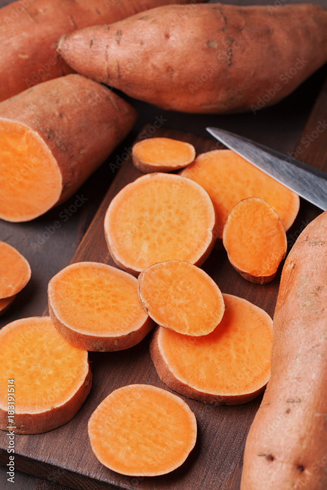 Fresh sweet potatoes whole and sliced on wooden kitchen board from above. Organic food. Fresh sweet potatoes whole and sliced on wooden kitchen board from above. Organic food.