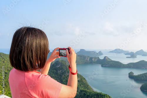 Woman tourist on peak viewpoint of Ko Wua Ta Lap island use camera take photos at beautiful nature landscape during sunrise over the sea in Mu Ko Ang Thong National Marine Park, Surat Thani, Thailand