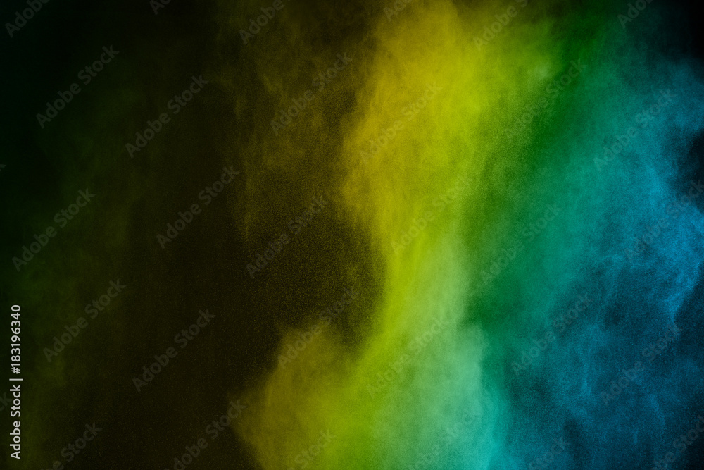 Abstract yellow green and blue powder splatter on black background,Freeze motion of color powder explosion. Splash of color dust on black background.