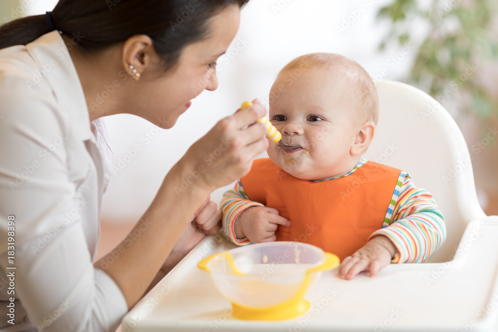 Φωτογραφία Food, child and parenthood concept - mom with puree and spoon feeding baby at ho