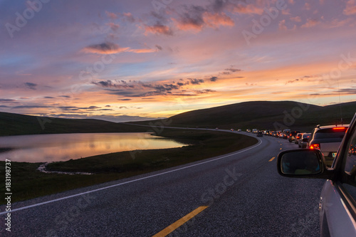A column of cars on a winding road at sunset, Mageroya island, Norway © natagolubnycha