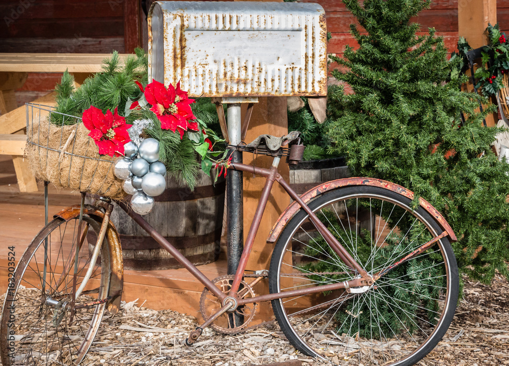 horizontal Christmas image of a very old rusty bike decorated with Christmas decoration and silver balls leaning against an old Tin mailbox.