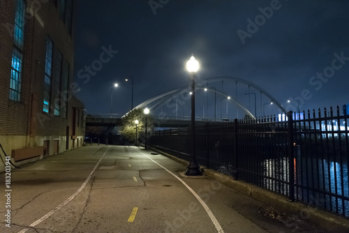 Riverwalk promenade and city bridge by an urban industrial building at the Chicago river at night.