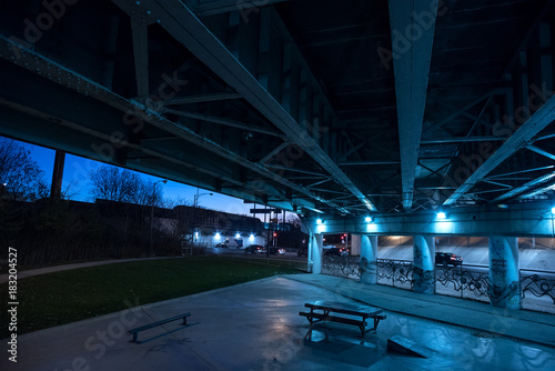 Obraz na plátne Gritty dark Chicago highway bridge underpass and city street with traffic and a bench at night