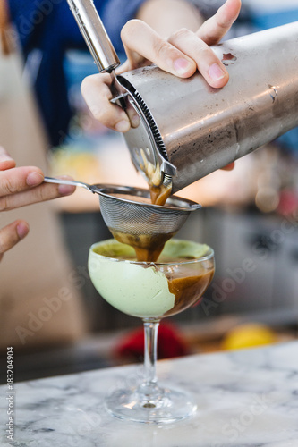 Bartender gently pour coffee mix with alcohol pass the filter in wine glass with green paste for making cocktail.