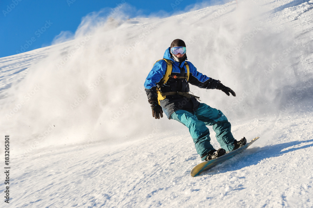 Freeride snowboarder rolls on a snow-covered slope leaving behind a snow powder against the blue sky Freeride snowboarder rolls on a snow-covered slope leaving behind a snow powder against the blue sky