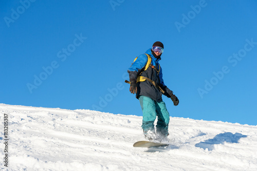 Freeride snowboarder rolls on a snow-covered slope leaving behind a snow powder against the blue sky