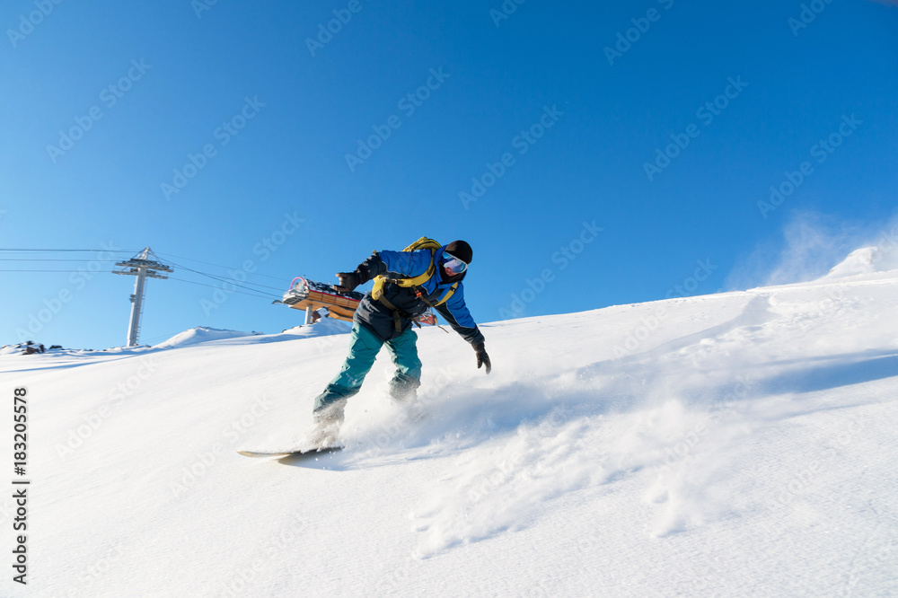 Freeride snowboarder rolls on a snow-covered slope leaving behind a snow powder against the blue sky Freeride snowboarder rolls on a snow-covered slope leaving behind a snow powder against the blue sky