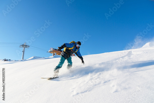 Freeride snowboarder rolls on a snow-covered slope leaving behind a snow powder against the blue sky